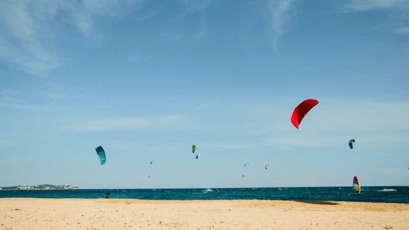 Kitesurfers above the water. Beach in foreground, windsurfer beneath the kitesurfers.
