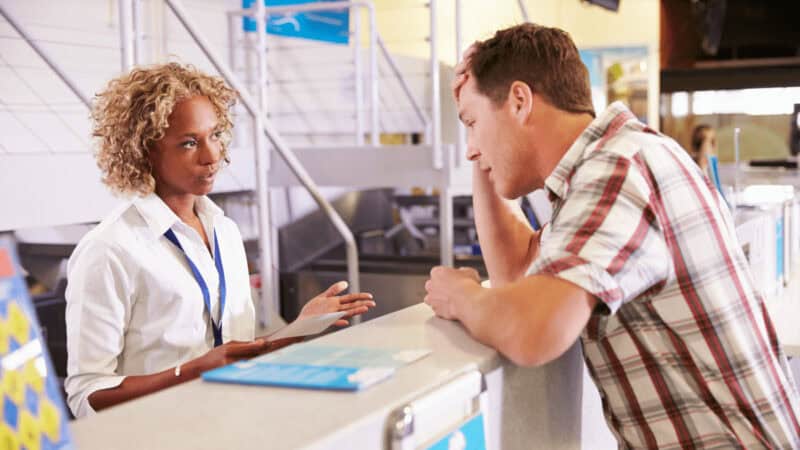 A gate agent explaining something to a frustrated man who's leaning on the counter.