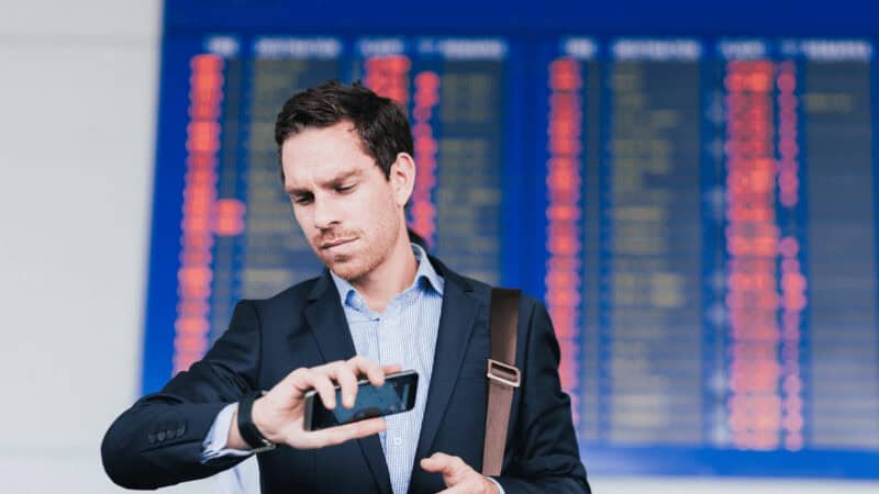 A man holding his cell phone and checking his watch at the airport.