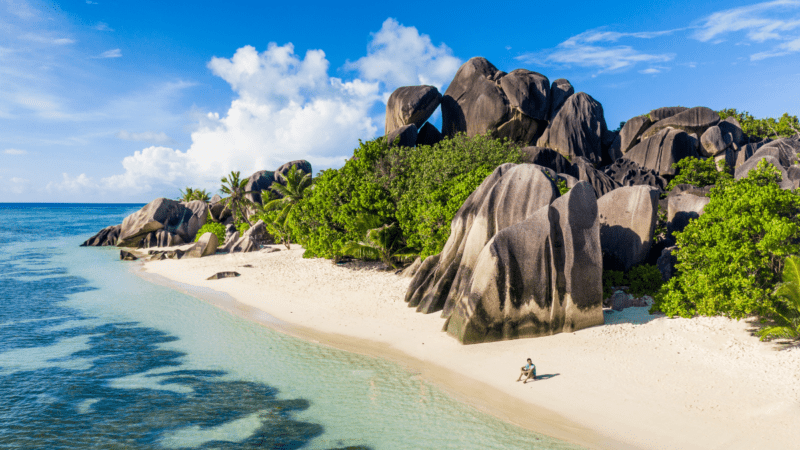 A person sitting on a beach at one of the most exotic holiday destinations on the planet: Anse Source d’Argent La Digue Island Seychelles