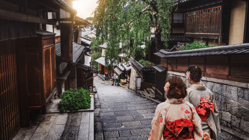 Two women in traditional Japanese garb walking down an old street in Kyoto Japan