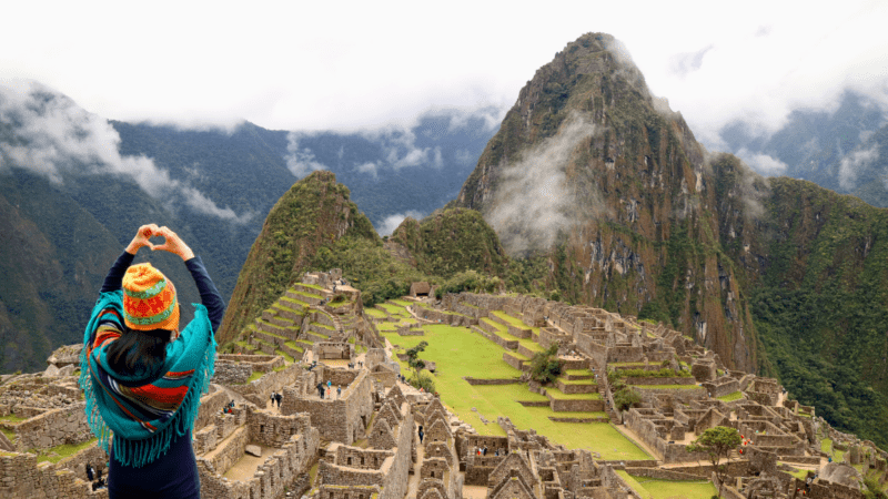 Female tourist gesturing a love sign to the ancient Inca ruins of Machu Picchu, Cusco, Peru