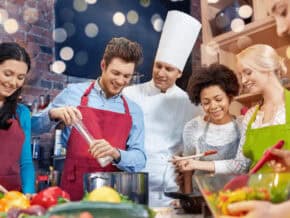 French chef behind five smiling students. Vegetables and other ingredients in the foreground.