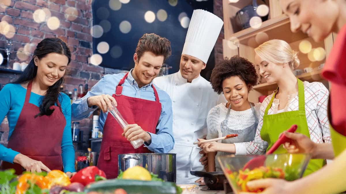 French chef behind five smiling students. Vegetables and other ingredients in the foreground.