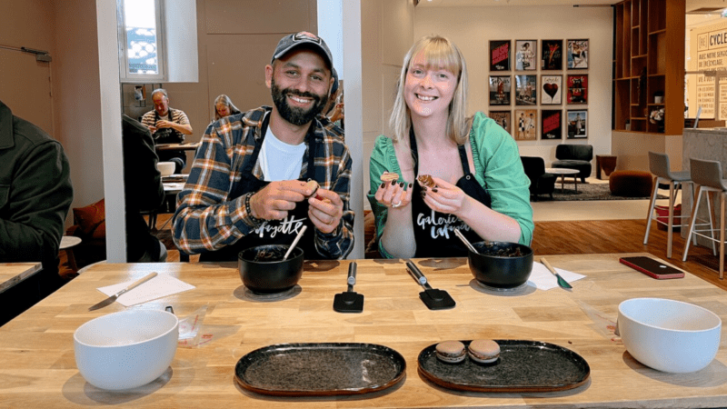 A man and woman smiling at the camera, while making macarons at a French pastry class.