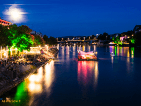 Night on the Rhine River in Basel Switzerland. People gather along the water to listen to a concert. Full moon in the sky.