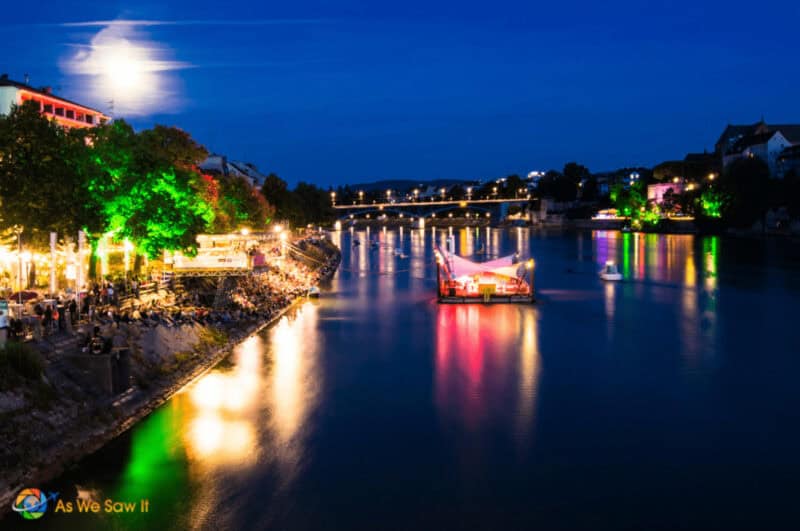 Night on the Rhine River in Basel Switzerland. People gather along the water to listen to a concert. Full moon in the sky.