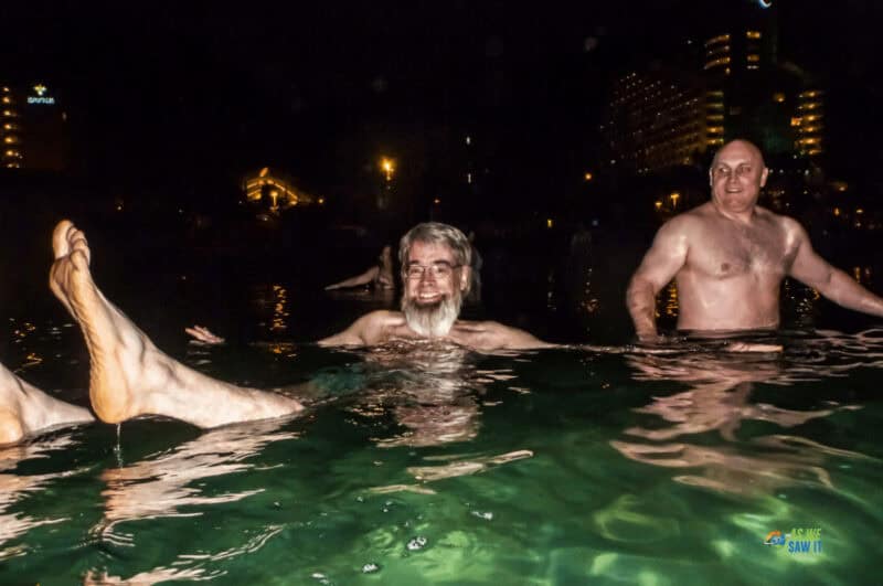 Three men swimming in the Dead Sea after dark