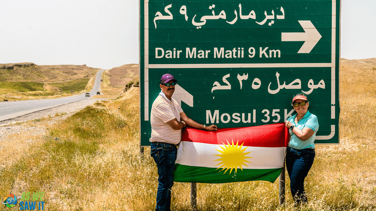 Couple holding a Kurdistan flag in front of a road sign to Mosul.
