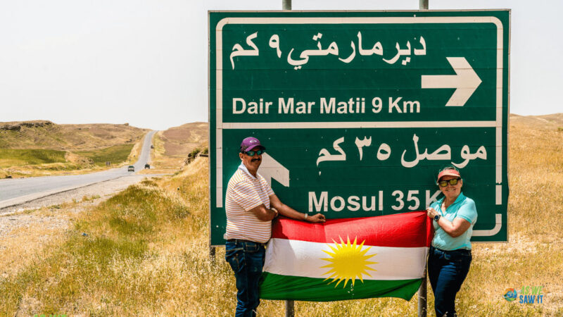My husband and I, holding a Kurdistan flag in front of a road sign to Mosul. Iraq is one of the most high-risk countries we've been to!