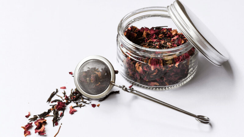 Tea infuser wand atop herbs along with a jar full of herbal tea.