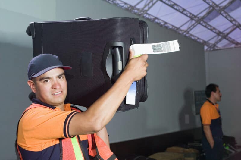 An airport worker carrying a suitcase on his shoulder