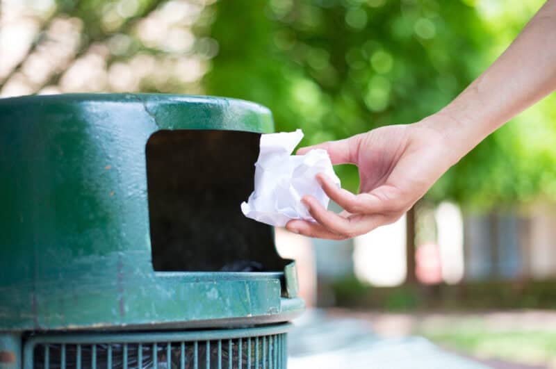 A hand throwing rubbish in a trash can