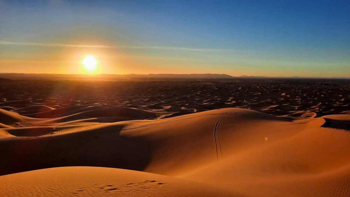 Sunset over rolling sand dunes in the Merzouga Sahara Desert.