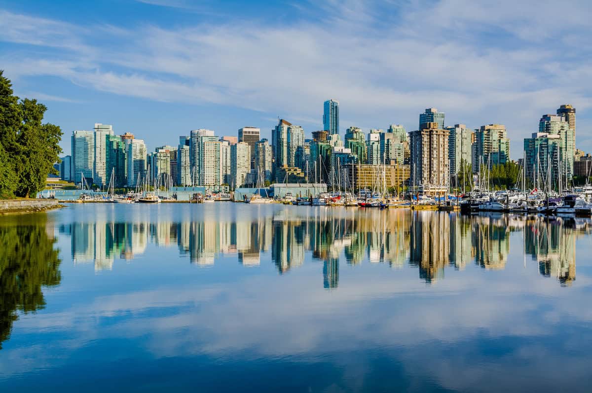 Modern city skyline with high-rise buildings and docked yachts reflected in tranquil waterfront near urban park