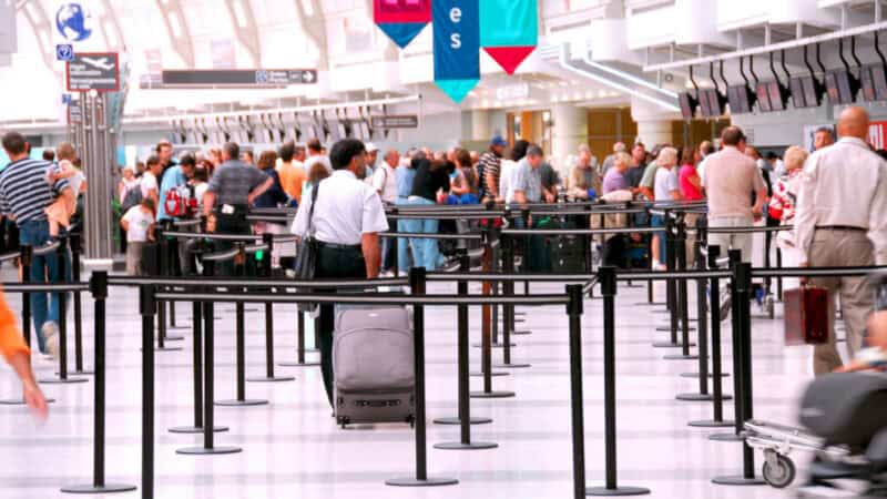 Travelers waiting in long airport security lines inside a busy terminal