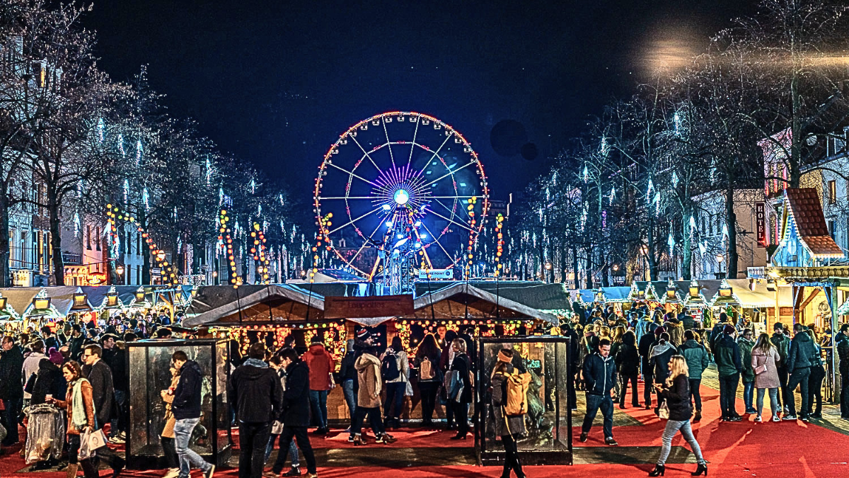 Brussels Winter Wonders Christmas market with wooden stalls and a Ferris wheel lit up at night.