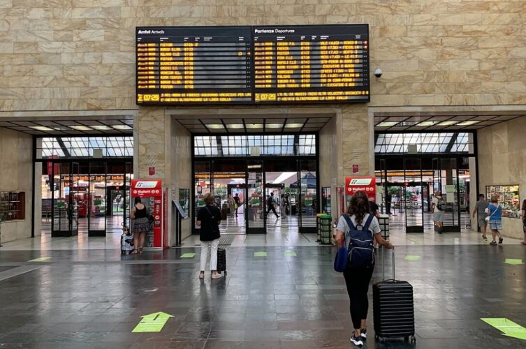 Traveler with luggage beneath the departure boards at Firenze Santa Maria Novella train station