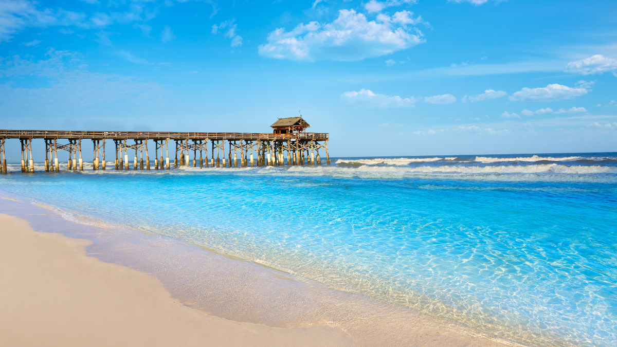 Sandy Florida beach with turquoise water and a long wooden pier extending into the ocean.