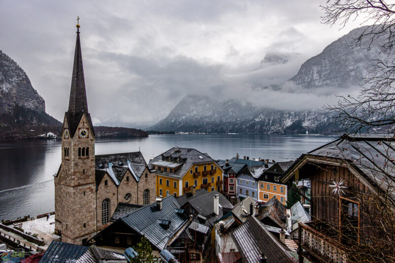 View over Hallstatt rooftops, church steeple, Lake Hallstatt, and snow-covered mountains in winter