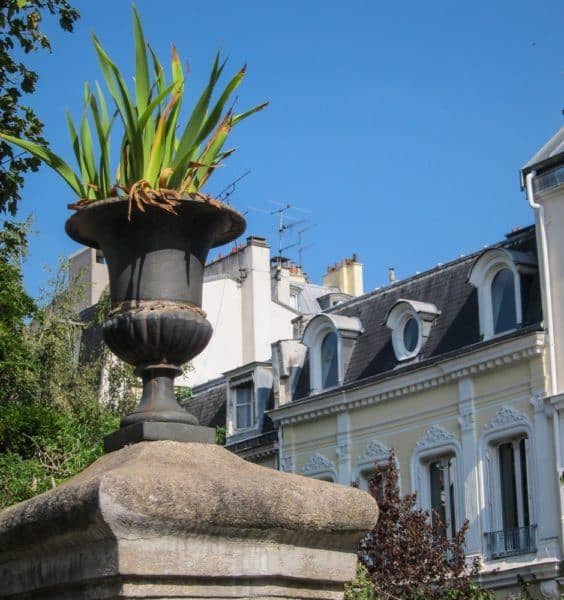 Urn on top of a wall in Cite des Fleurs, with a pretty building behind it