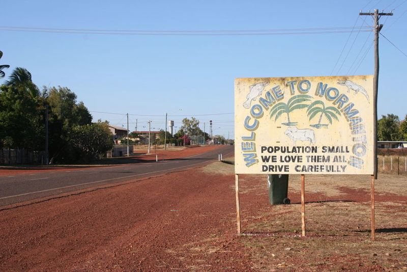 Sign along the road outside one of the towns in the Australian outback. Says Welcome to Normanton Population small we love them all. Drive Carefully.