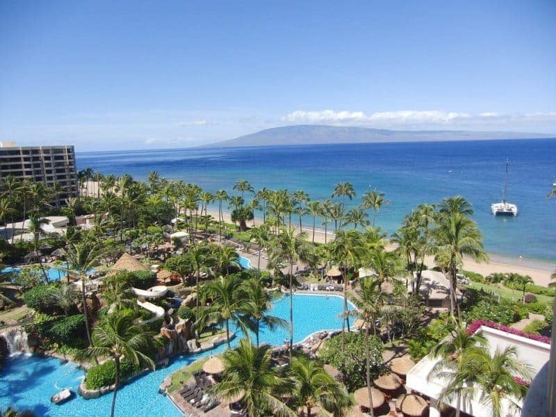 Pool, palm trees, sandy beach and ocean at a Hawaii resort. Mountain in background.